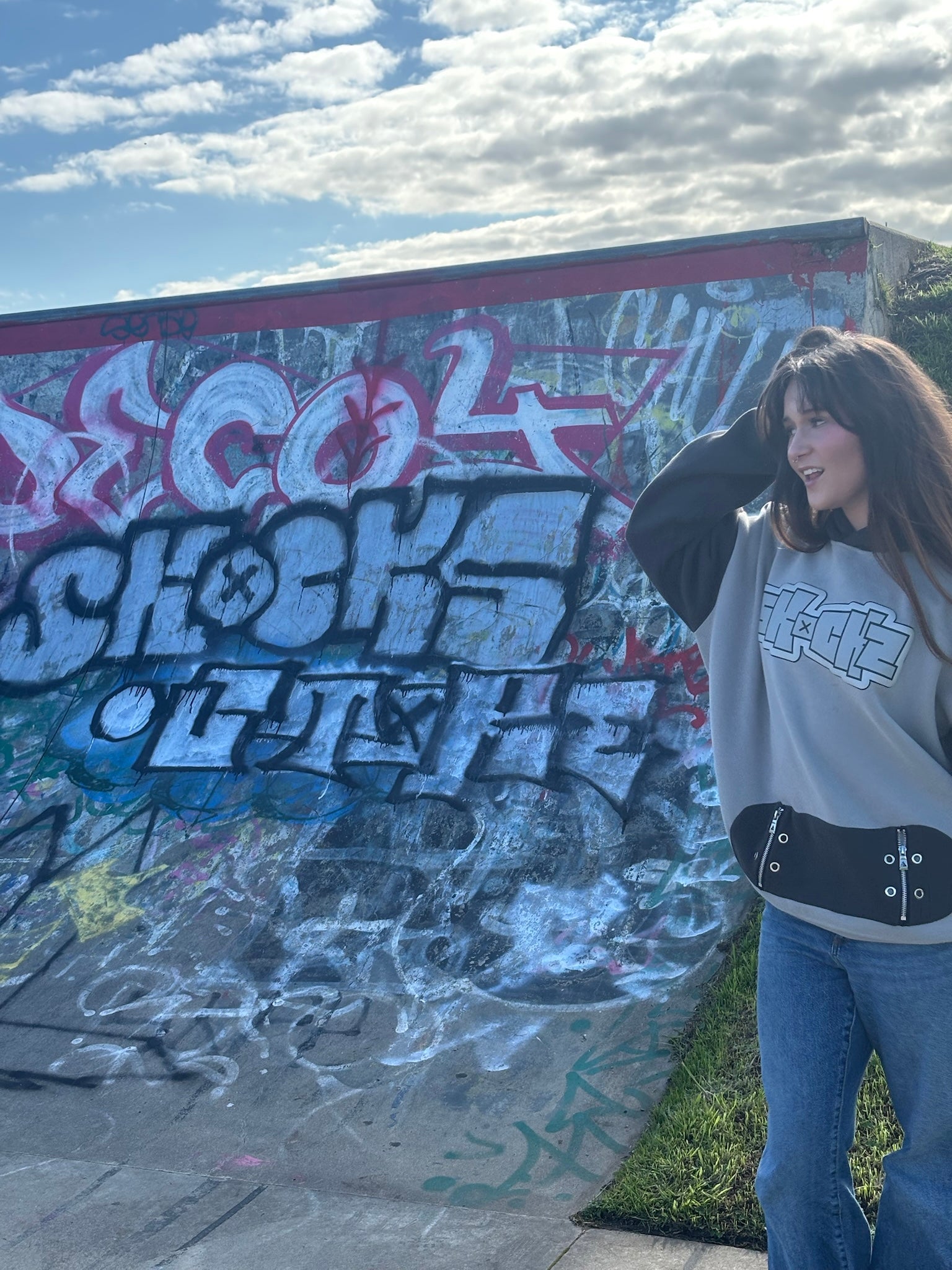 SKOCKZ Signature Hoodie worn side-on beside a graffiti skate ramp, showing the boxy fit and hem hardware